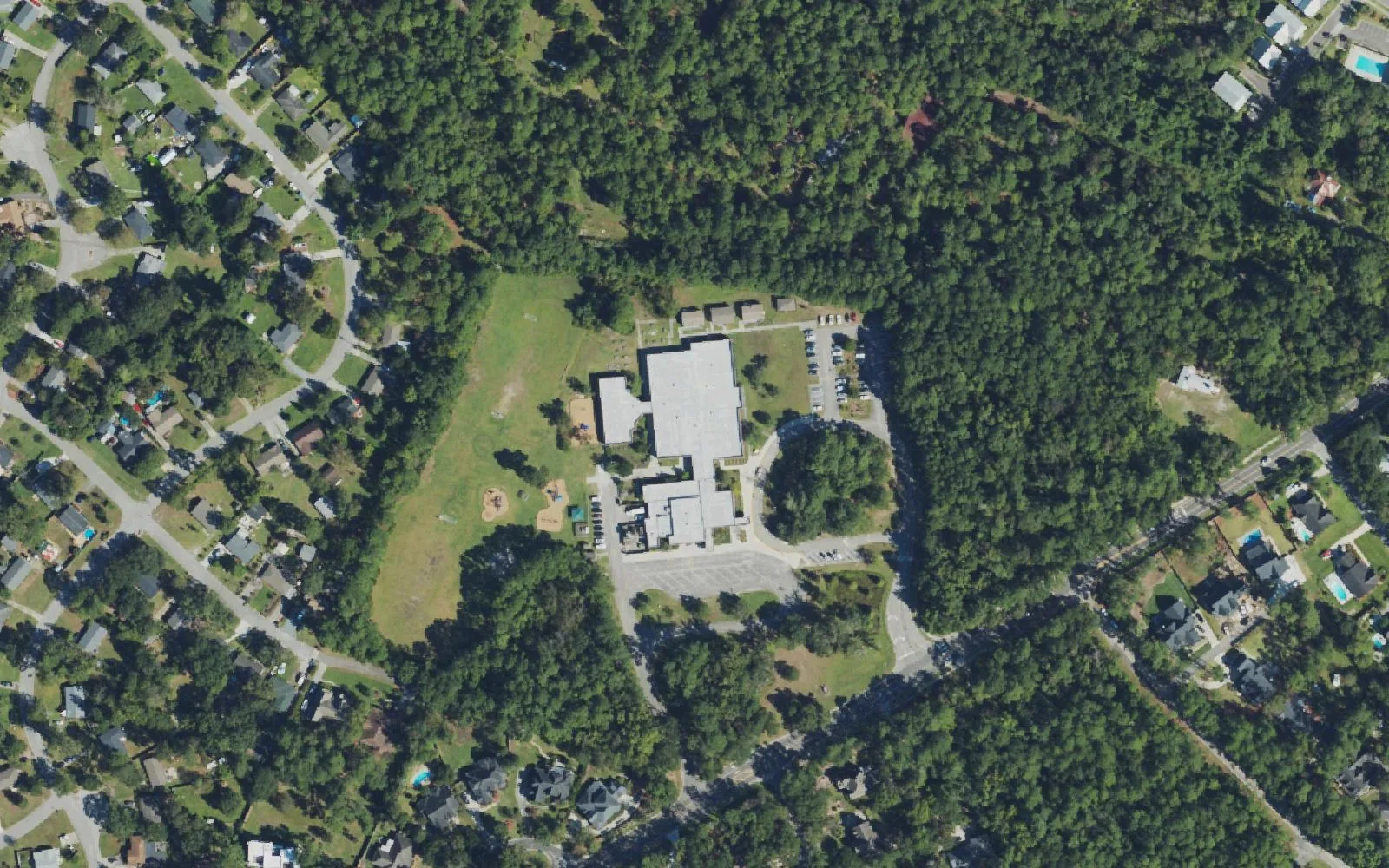 Bradley Creek Elementary School and its playing field off Greenville Loop Road in Wilmington, seen from the air, surrounded by woods and homes