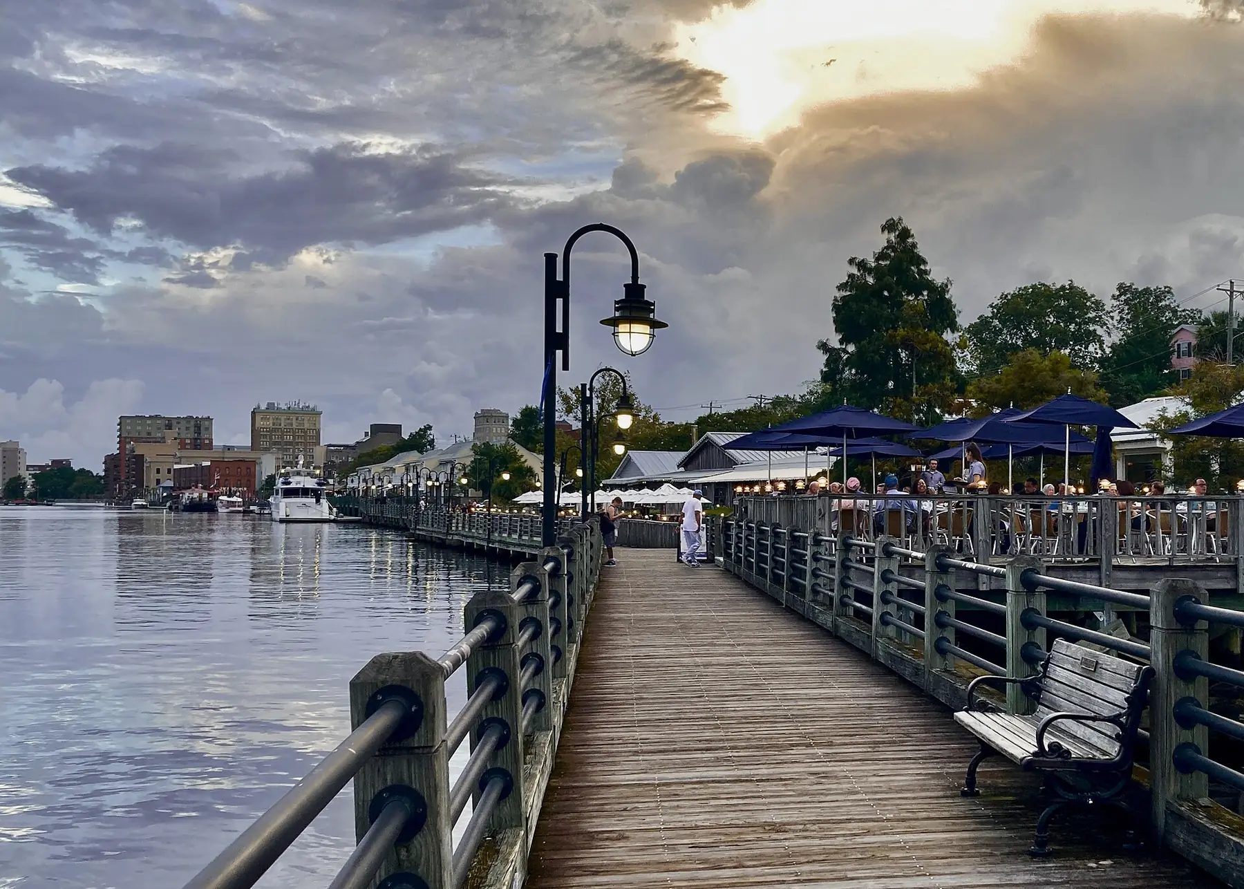The Riverwalk along the Cape Fear River in downtown Wilmington at sunset, with riverside dining on the right.